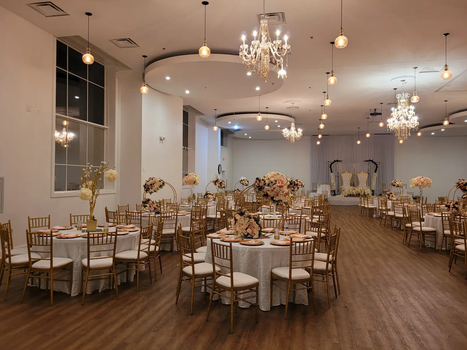 Fellowship hall in the evening with warm lighting, round tables with floral centerpieces, and crystal chandeliers