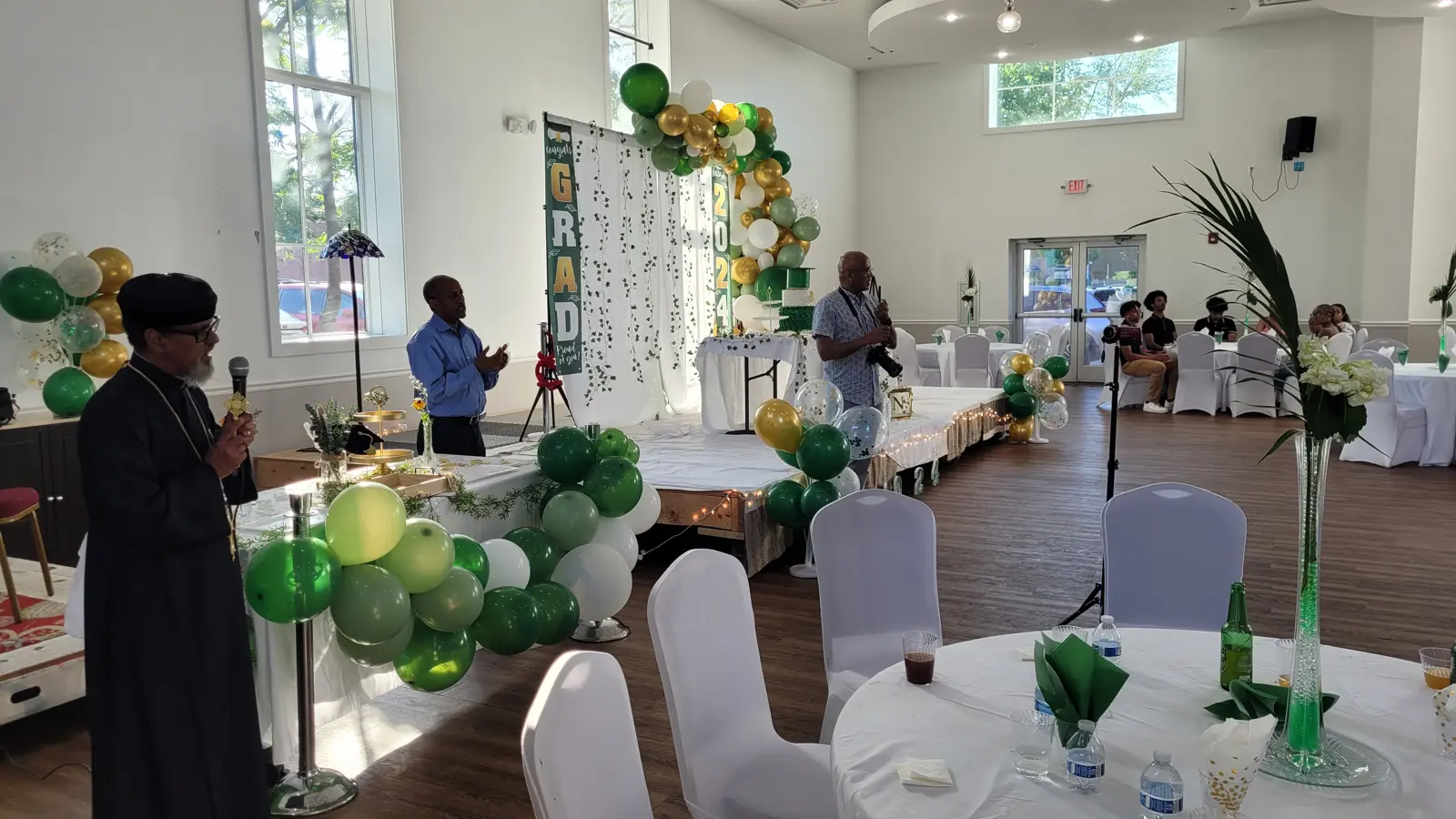 Graduation celebration with green and gold balloon arches and decorated round tables